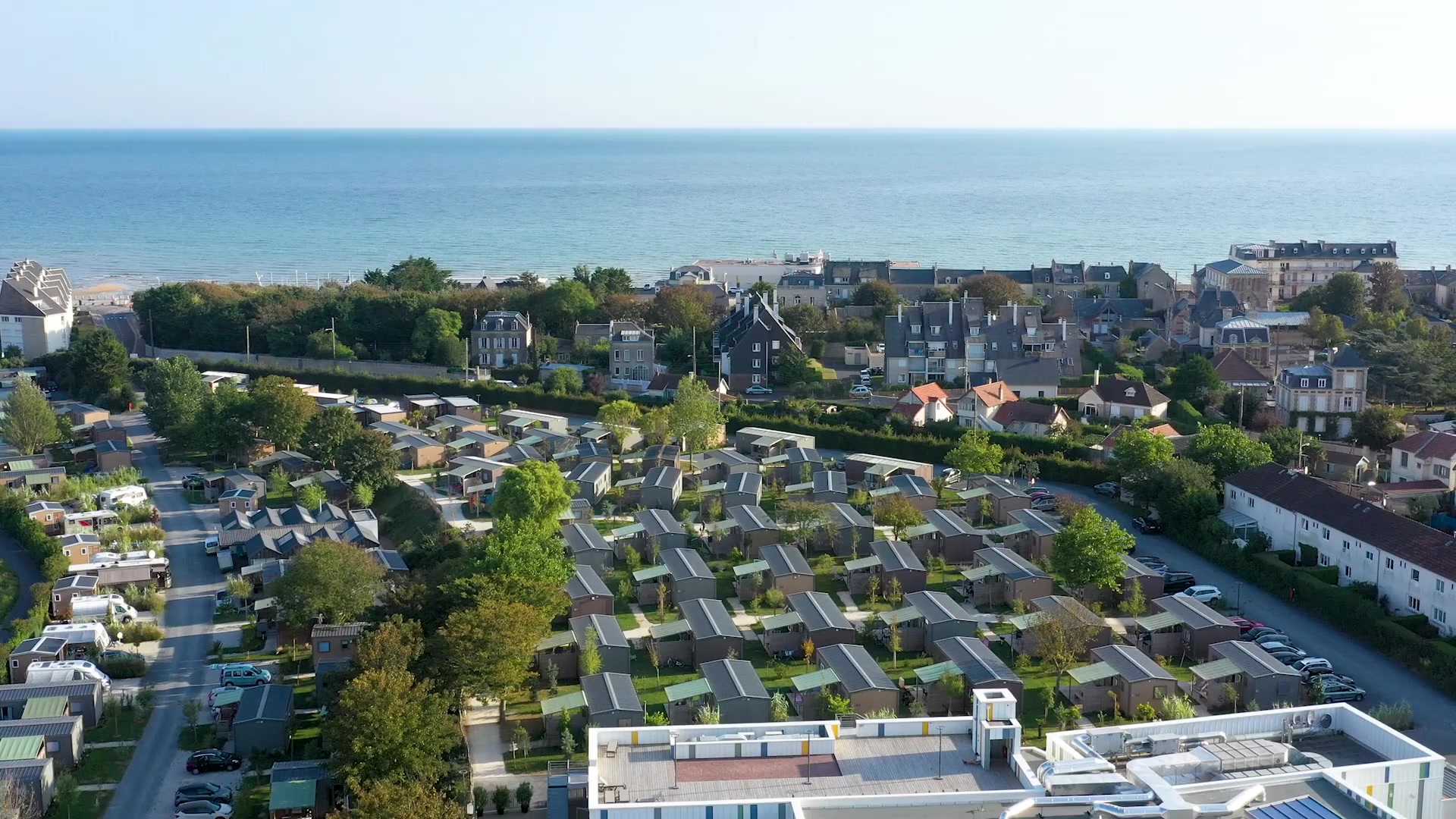 Der Campingplatz La Capricieuse aus der Luft: Cottages im Grünen, dahinter direkt das Meer, in Luc-sur-Mer