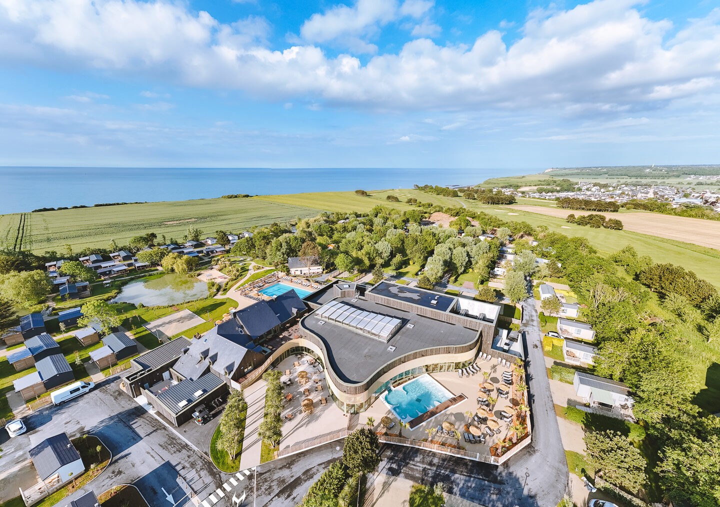 Le camping Portland vu du ciel : l’espace aquatique, l’étang et la Manche, Port-en-Bessin à l’horizon